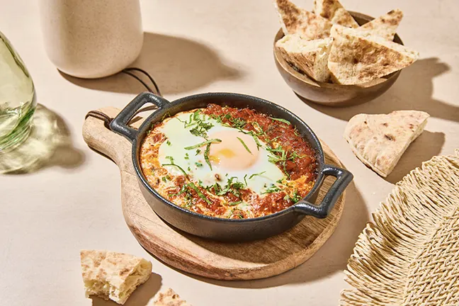 Chakchouka à l'œuf servie dans son poêlon, avec du pain pita